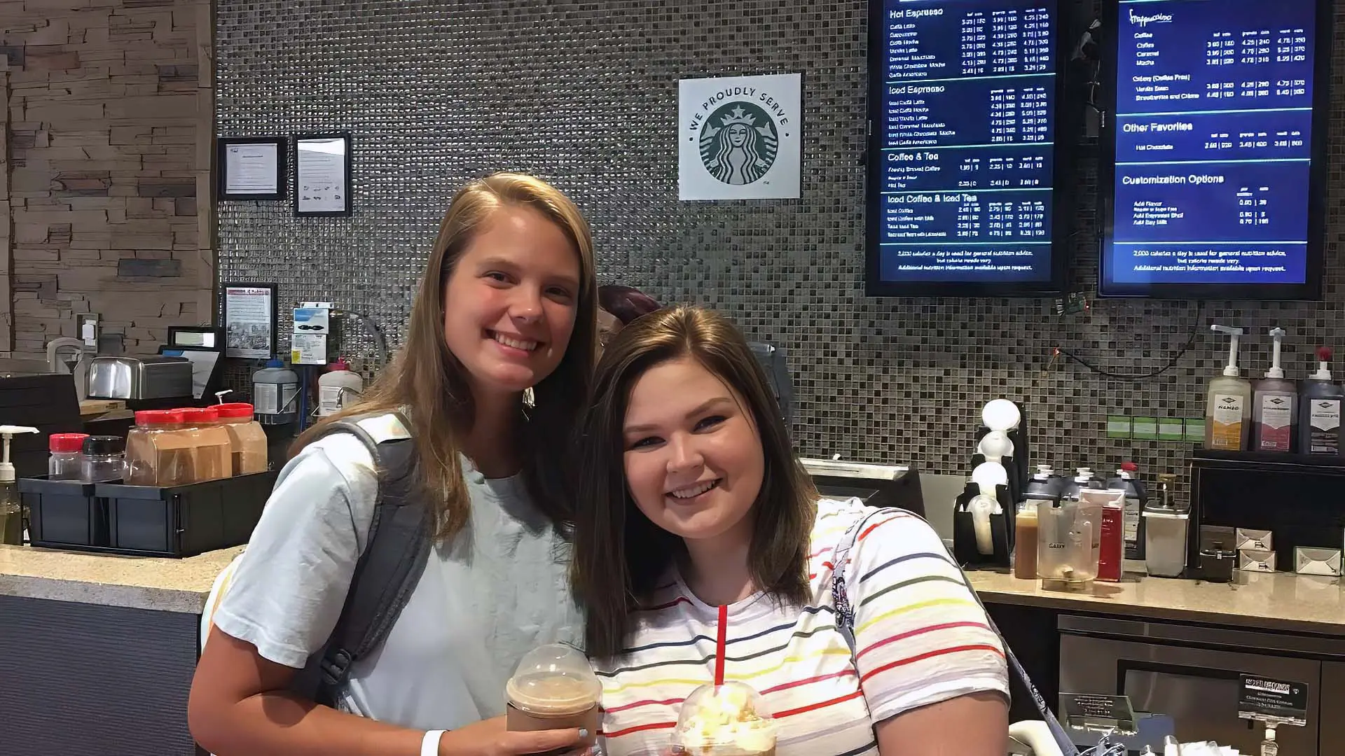 Two students smiling while standing in front of coffee shop holding drinks